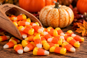 Tri-coloured sweets spilling from a wooden scoop onto a rustic autumn table.
