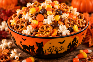 Orange Halloween bowl filled with popcorn, pretzels, chocolate candies and colourful sweets.