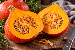 Red Kuri squash cut open to reveal bright golden-orange flesh, pale seeds and a thin reddish-orange rind on a rustic cutting board.
